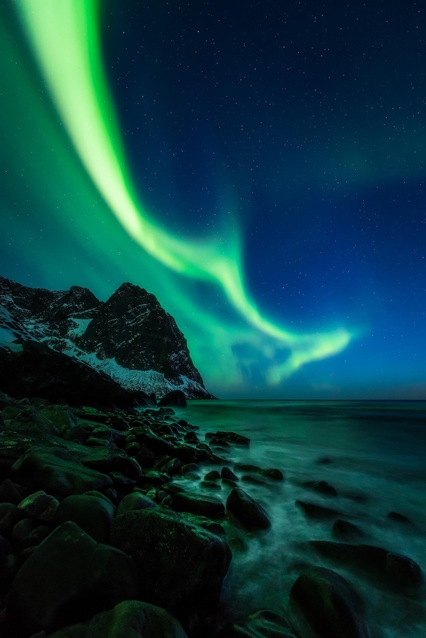 Green flames on the blue vernal night sky and grumbled pieces of the mighty mountains pounded and shaped by the endless great open ocean waves Lofoten Norway   mpxmark