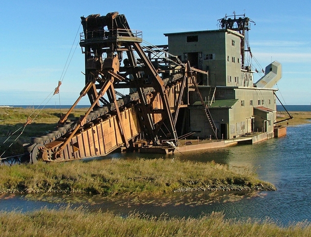 I saw a few abandoned dredgers in Alaska but this was the biggest by far located just outside of Nome near-arctic Alaska  The tail boom is also massive though its not clear from this angle Each scoop on the belt is the size of an arm chair The interior wa