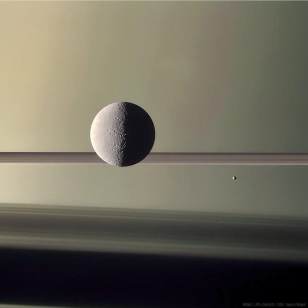 Thats Rhea Saturns second-largest moon and Epimetheus the smaller moon to the right against a backdrop of Saturn its rings and ring shadows