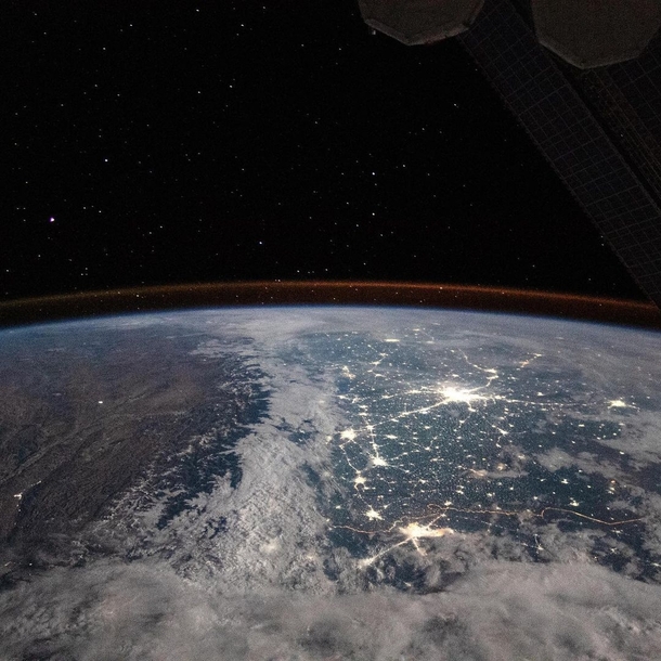 The snow-covered Himalayan Mountains and the bright city lights of New Delhi India and Lahore Pakistan are also visible below the faint orange airglow of atmospheric particles reacting to solar radiation taken from the International Space Station