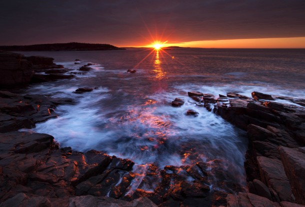 The suns rays strike the rocky coast of Acadia National Park Maine 