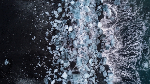 Top down shot of waves crashing against the ice onthe black sands of Breiamerkursandur also known colloquially as Diamond Beach in the South of Iceland   x 