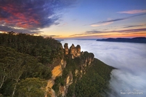 A cloud inversion fills the Jamison Valley as sunrise lights up the sky at The Three Sisters in Katoomba in The Blue Mountains 