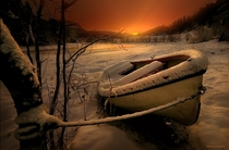 Old row boat tied off at the rivers edge in a winter landscape with a sunset in the background Photo by Wim Lassche 