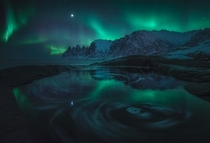 The Aurora reflecting in a swirling tide pool Senja Norway 