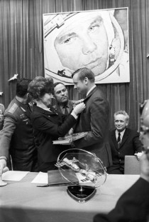 Valentina Tereshkova first woman in space holds Neil Armstrong first man on the moon by the cuff while Yuri Gagarin first man in space looks down on them from the wall in  