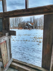 View of an abandoned farmhouse from inside the barn