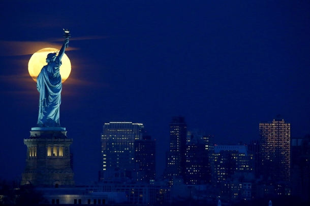 A full moon rises behind the Statue of Liberty seen from the Port Liberte neighborhood of Jersey City New Jersey Julio Cortez 