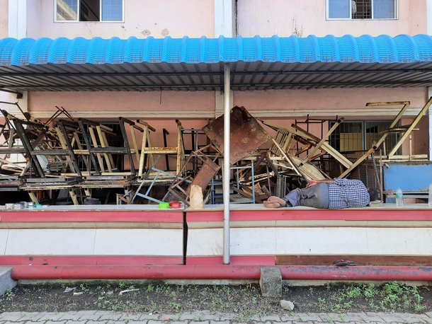 A man takes a siesta near a pile of abandoned furniture in my university campus 