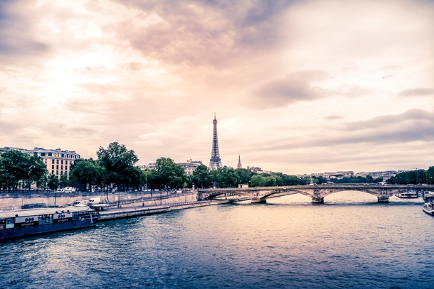 An iconic Eiffel Tower looms over the Seine on a cloudy summers day 