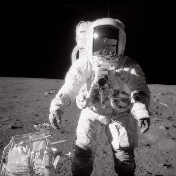 Astronaut Alan L Bean Lunar Module pilot pauses near a tool carrier during extravehicular activity EVA on the Moons surface Commander Charles Conrad Jr who took the black and white photo is reflected in Beans helmet visor -- November   