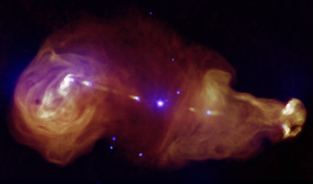 C showing jets generated by a supermassive black hole at the center of the galaxy where the galaxy is seen as a tiny point at the center of the giant plumes Composite image from observations by Chandra and the VLA 