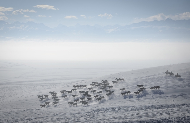 Herders ride horses on snow-covered field in Zhaosu County Yili Xinjiang Uighur Autonomous Region China