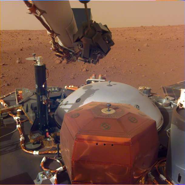 Image from InSights robotic-arm mounted Instrument Deployment Camera shows the instruments on the spacecrafts deck with the Martian surface of Elysium Planitia in the background