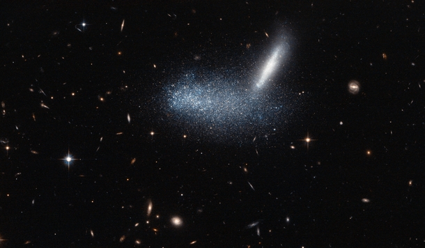 In the foreground the irregular dwarf galaxy PGC   seen here as a cloud of stars  covers its neighbouring galaxy which appears edge-on as a streak 