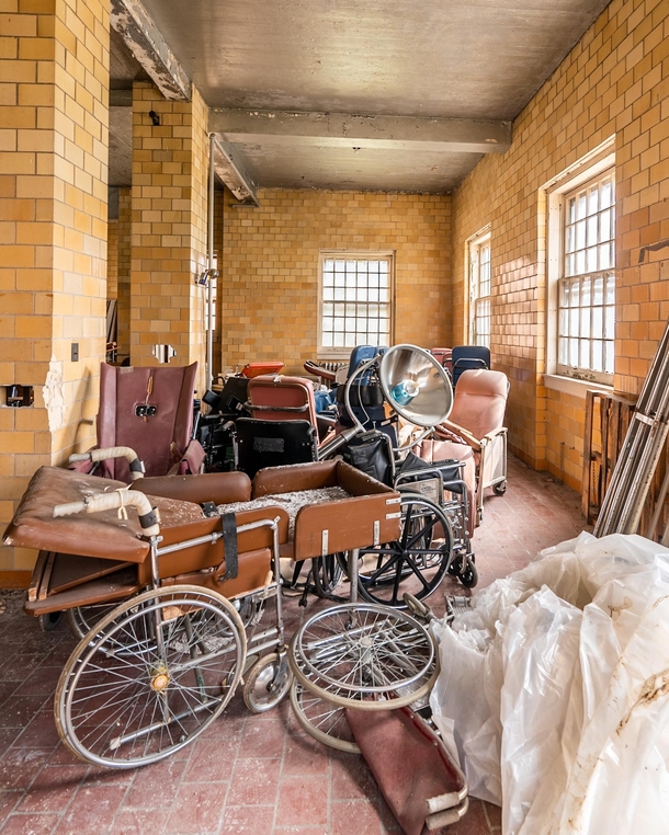Old wheelchairs piled in a corner of a room inside an abandoned state hospital 