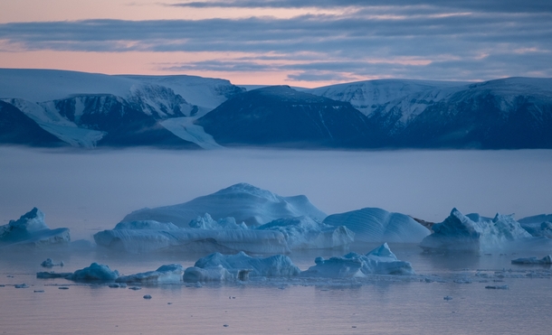 Pink skies glaciers feeding into the sea pale blue icebergs and majestic fog moving into the bay at sunset as seen from my window in the far north Qaanaaq Greenland 
