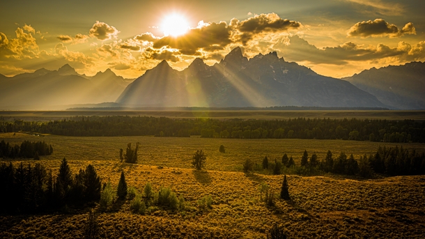 Setting sun painting the landscape behind the Grand Tetons Jackson WY 