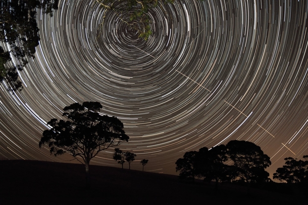 The International Space Station ISS appears to pierce a path across the radiant concentric star trails seemingly spinning over the silhouettes of the trees in Harrogate South Australia by Scott Carnie-Bronca 