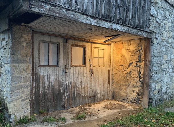 This abandoned stone barn is located in an alley in my hometown Overall its in a bad state of disrepair but the entryway is still illuminated by an old solitary incandescent lightbulb