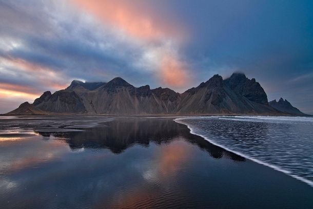 Waves roll in on a black sand beach beneath a midnight sunset Vestrahorn Iceland 