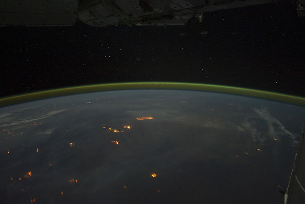 Wildfires with smoke plumes faintly visible in the night sky of Australia the gold green halo is atmospheric airglow hanging above the horizon 