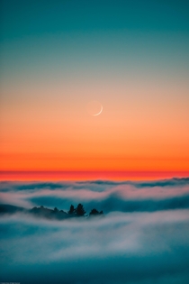 A crescent moon setting over fog
