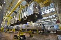 A gleaming New York City subway car hanging from the ceiling gantry crane during scheduled maintenance at Coney Island Yard 