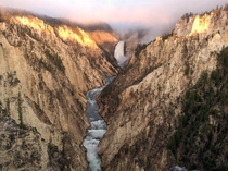 Fog on top of the Lower Falls of the Yellowstone with the morning sun lighting up the Canyon walls 