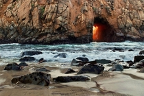 Sunset glows behind sea cave entrance Pfeiffer Beach Big Sur California 