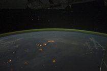 Wildfires with smoke plumes faintly visible in the night sky of Australia the gold green halo is atmospheric airglow hanging above the horizon 